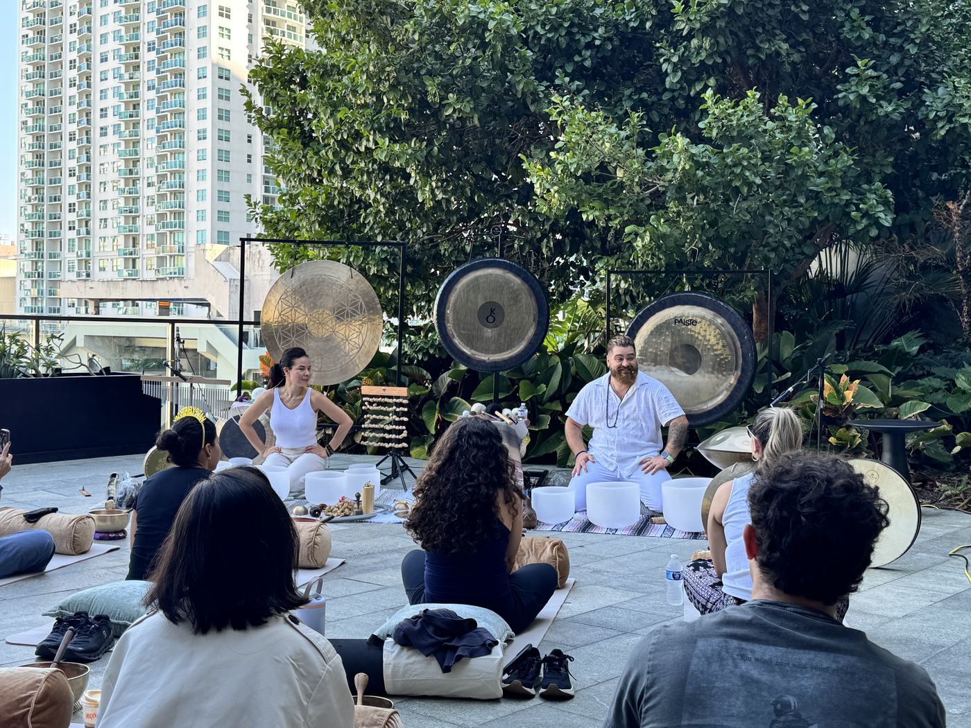 A group seated on cushions facing the gongs