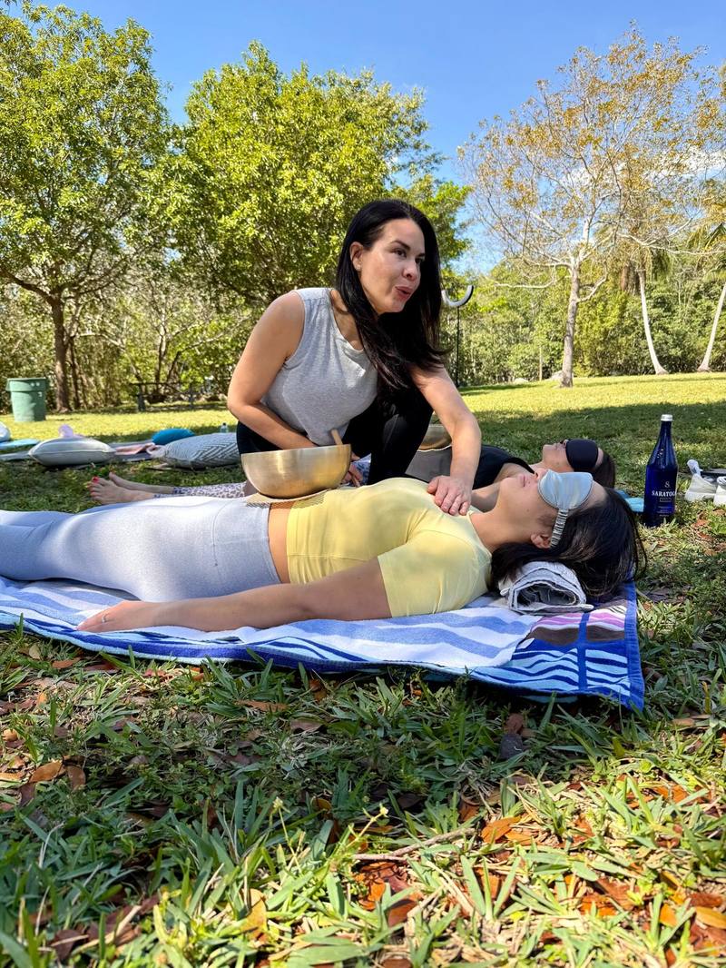 Karina playing a singing bowl over a guest at rest in the park