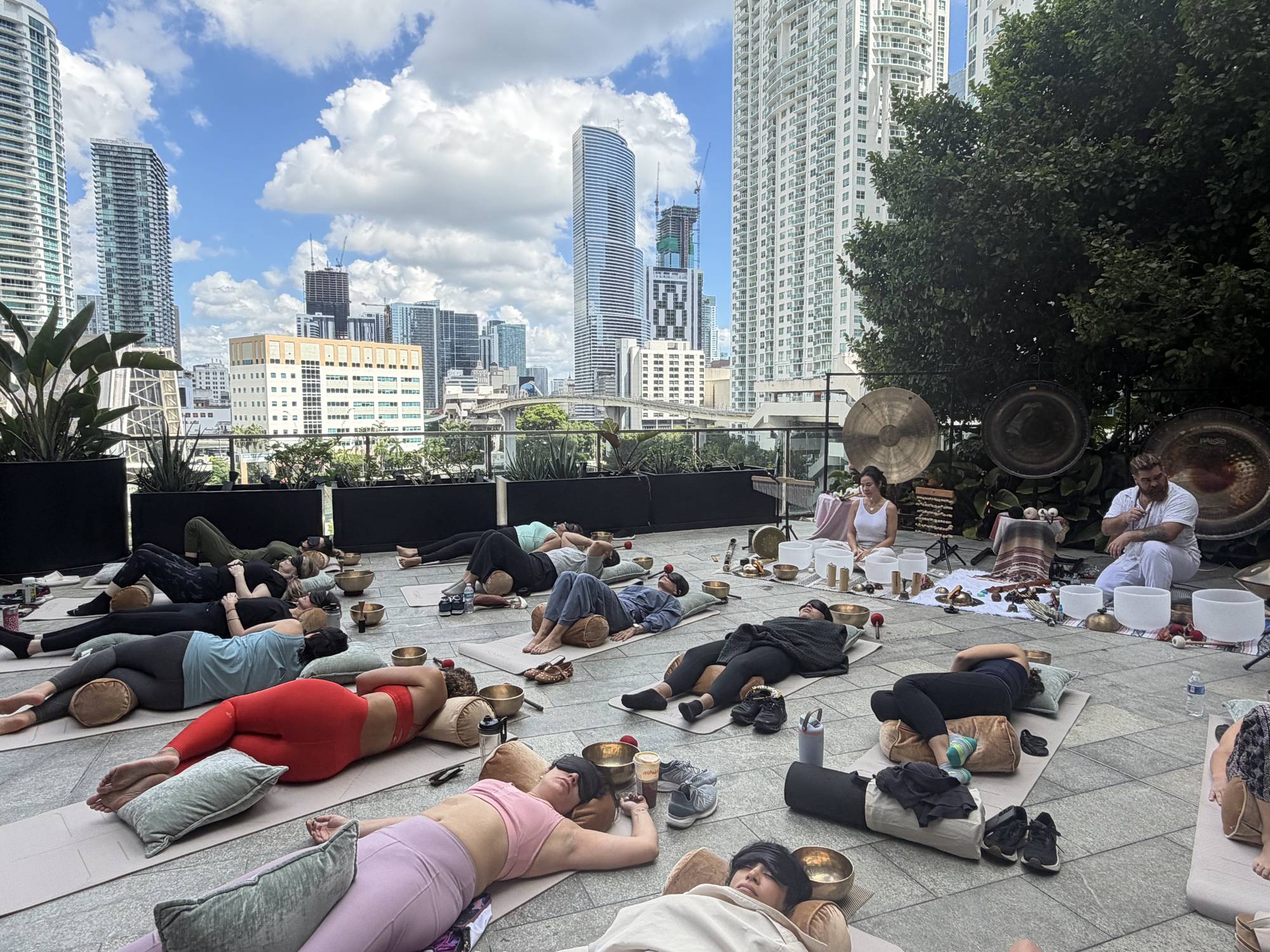 People resting on mats on the Puttshack terrace, Brickell towers above